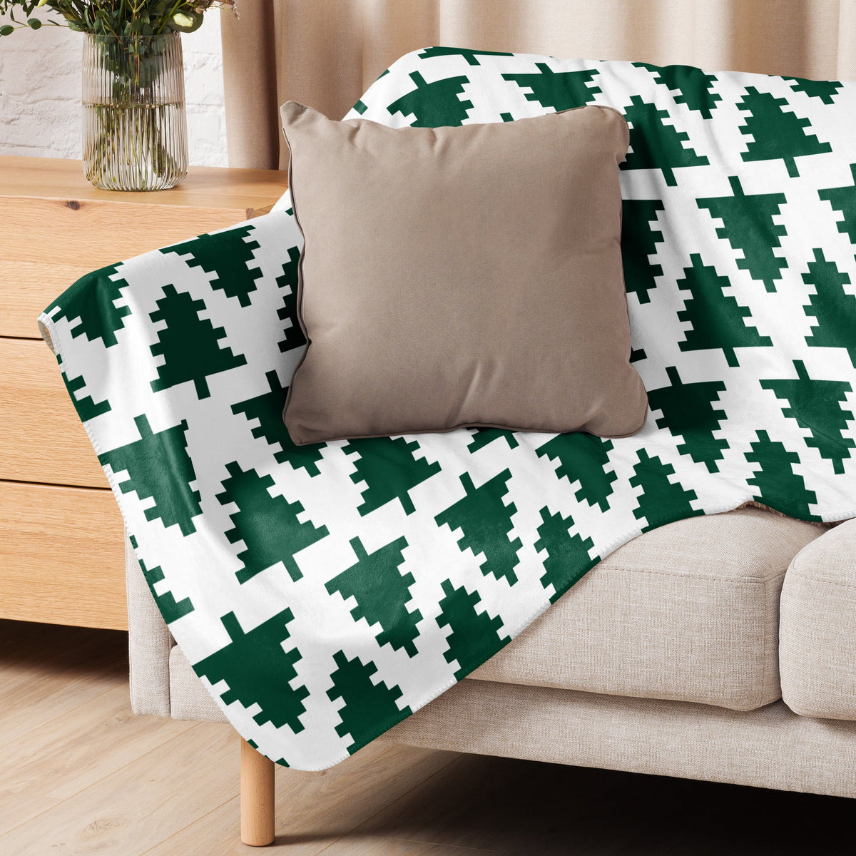 A cozy white Christmas blanket with dark green pixelated pine trees draped over a beige sofa