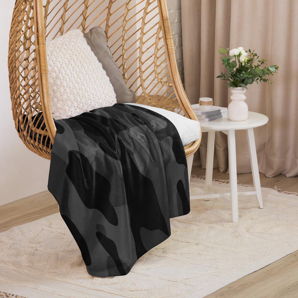 Black camo blanket with camouflage pattern draped over wicker hanging chair for cozy outdoor use