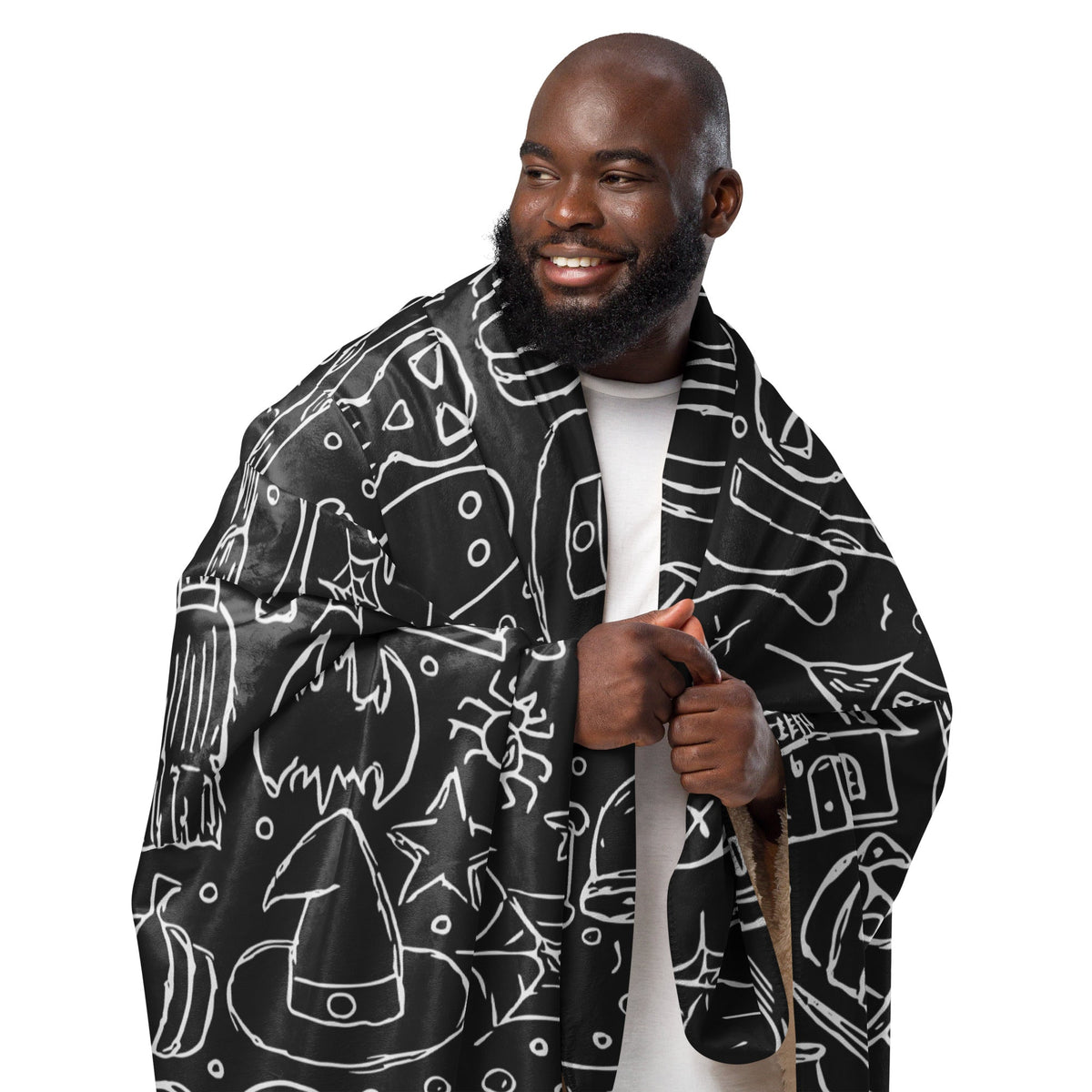 Black halloween blanket with white line-drawn halloween illustrations draped over a man’s shoulders