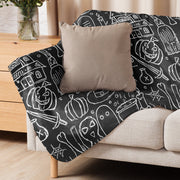 Black halloween blanket with white chalk style halloween illustrations draped over a beige couch