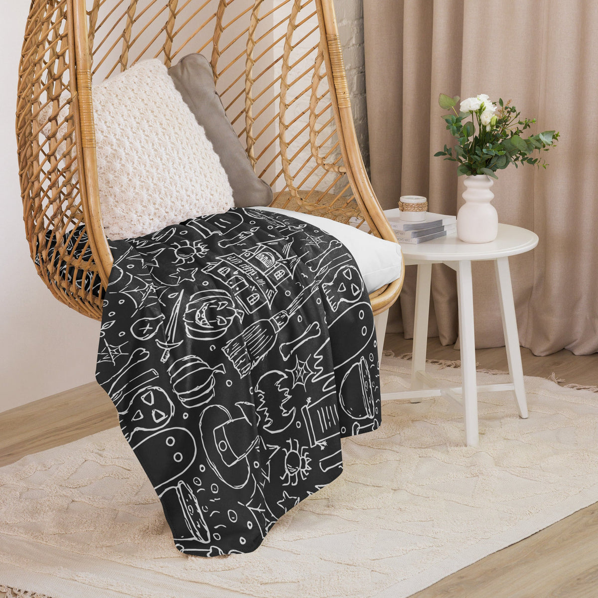 Black halloween blanket with white chalk-style illustrations draped over a wicker chair for spooky decor