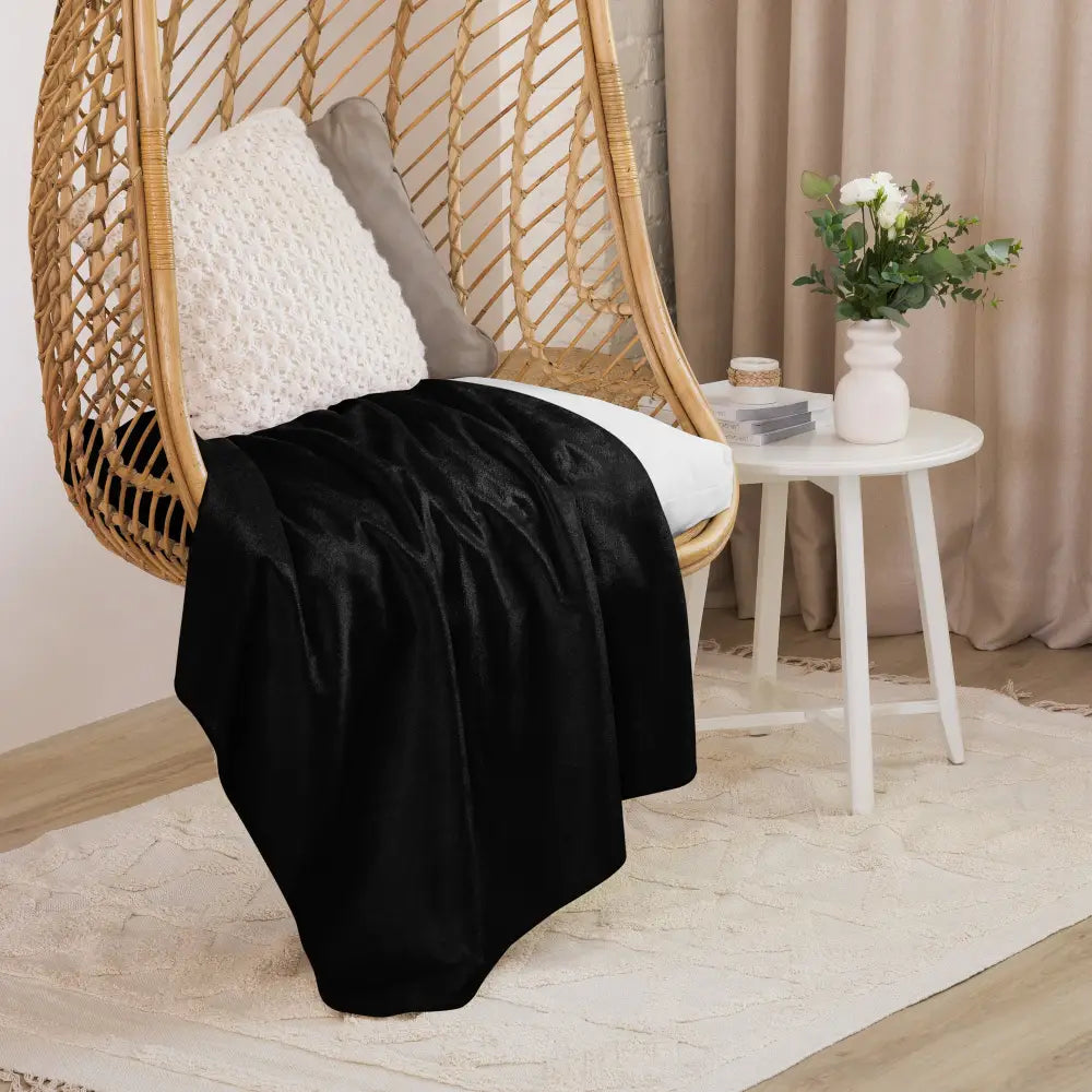 Black sherpa blanket in black velvet draped over a wicker hanging chair for cozy indoor use