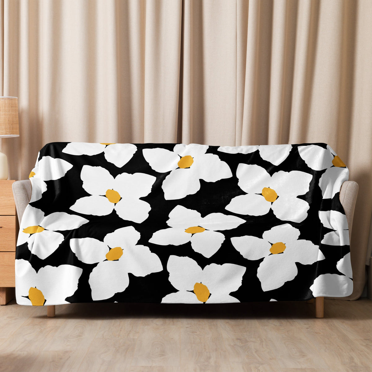 Black and white floral blanket with bold white flowers and yellow centers on a soft black fabric