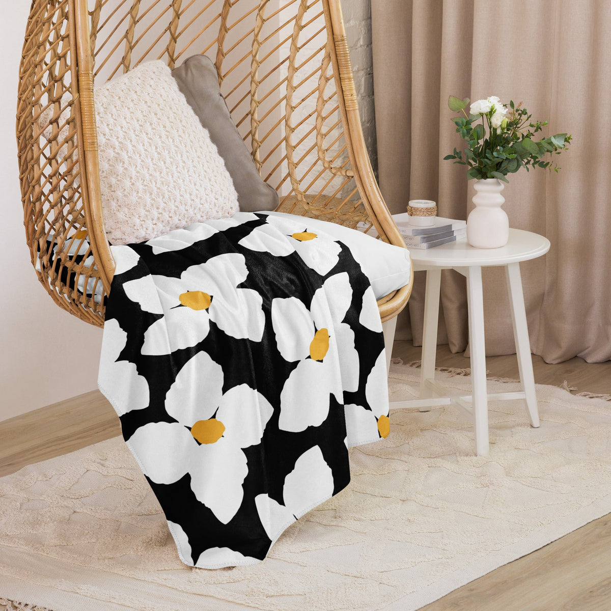 Black and white floral throw blanket with yellow centers draped over a wicker hanging chair for cozy decor