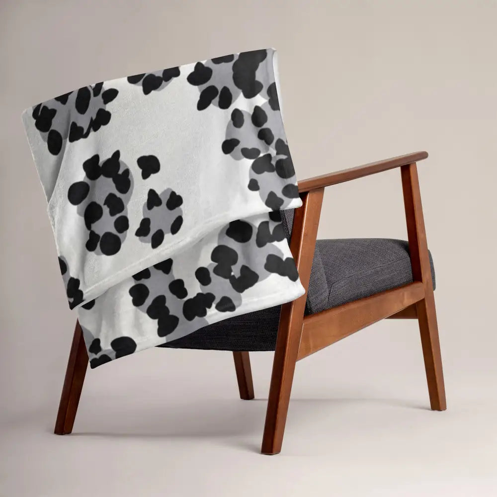 A soft white blanket with bold black and gray paw print pattern draped over a wooden armchair back side