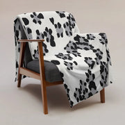 A cozy black and white leopard print blanket with black and gray paw prints draped over a wooden armchair
