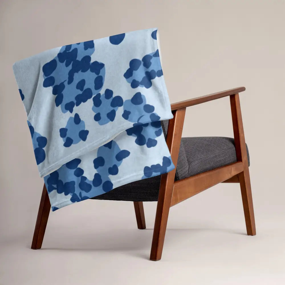 Une couverture bleue léopard en douceur bleu clair avec des motifs floraux abstraits bleu foncé sur un fauteuil en bois