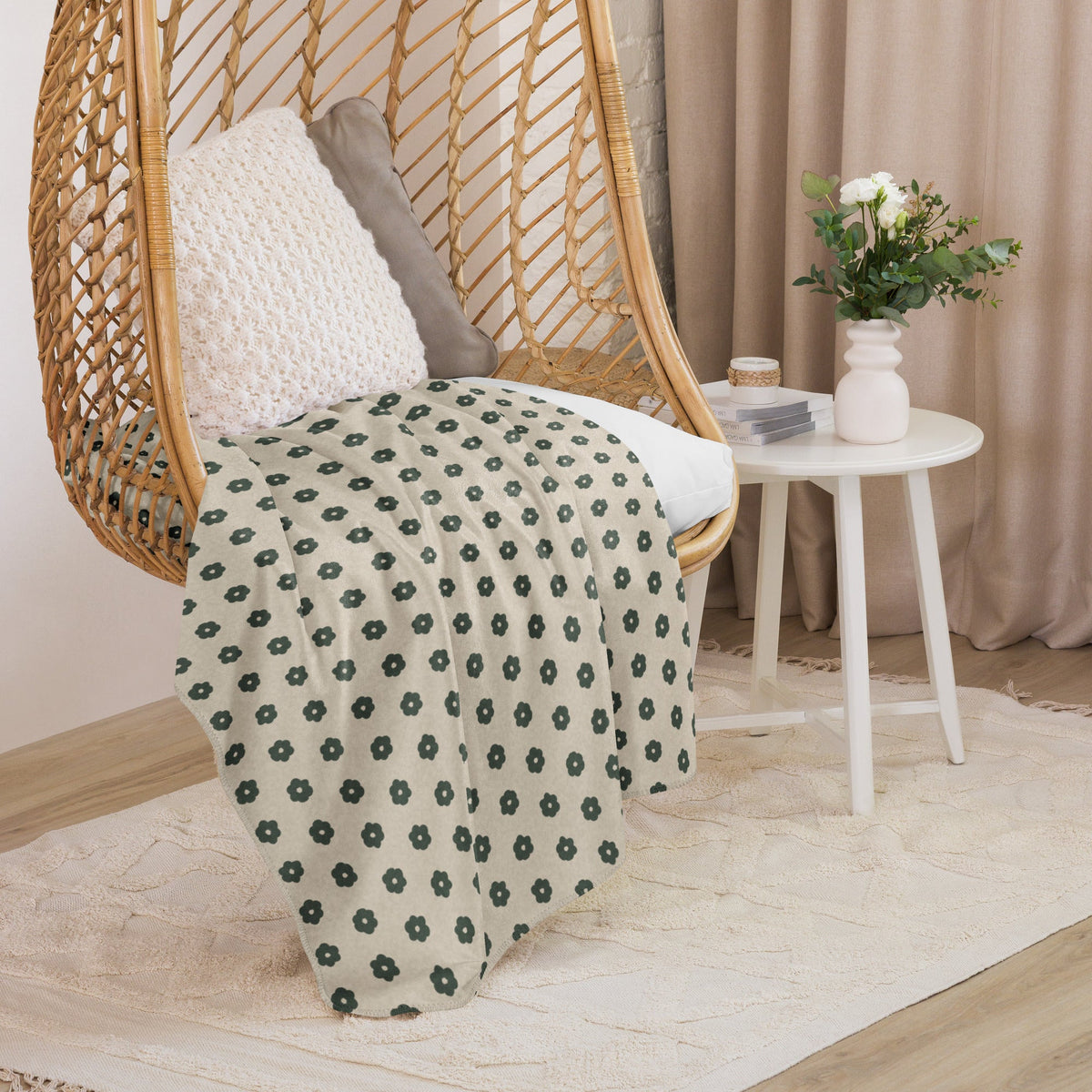 A soft cream-colored boho floral blanket with dark green flower patterns draped over a wicker hanging chair