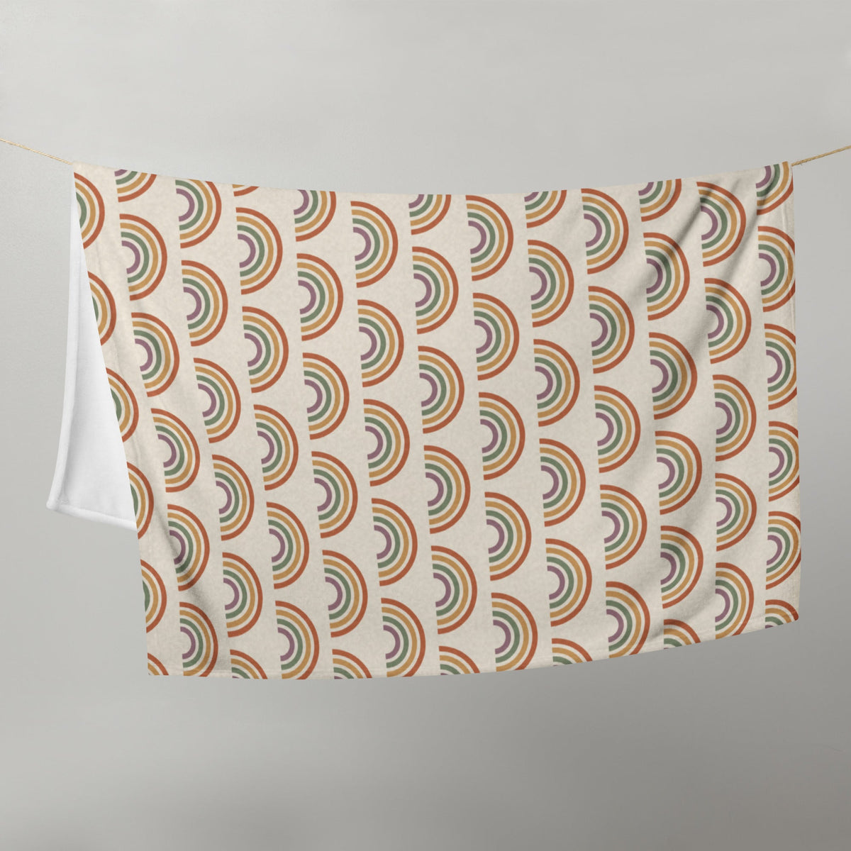 A cream-colored boho rainbow throw blanket with a vintage-style repeating rainbow pattern in earthy tones