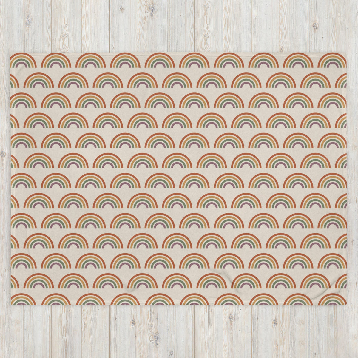 A soft cream-colored boho rainbow throw blanket with vintage-style rainbows in muted earth tones