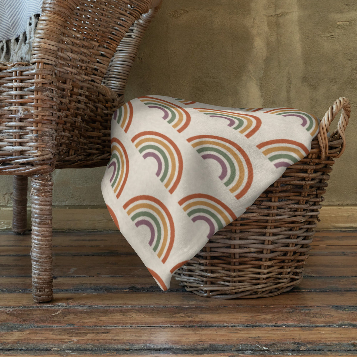 A soft cream-colored boho rainbow throw blanket with colorful orange green and purple stylized rainbows pattern