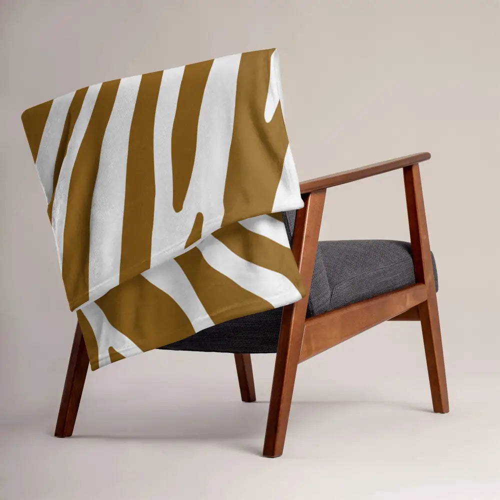 Couverture marron imprimé zèbre avec larges rayures verticales dorées et blanches, douce et cosy sur fauteuil en bois