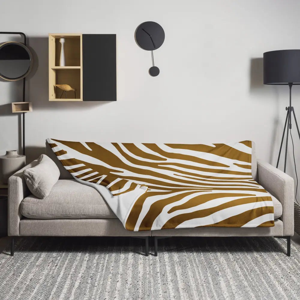 Une couverture marron à motifs zèbre dorés et blancs drapée sur un canapé gris moderne, avec une texture douce