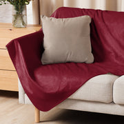 A plush deep red velvet sofa cover draped over a light couch with a beige pillow for burgundy sherpa blanket use