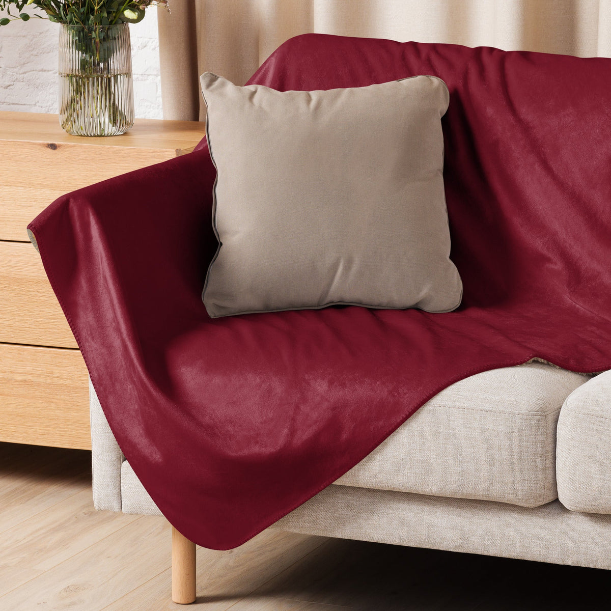 A plush deep red velvet sofa cover draped over a light couch with a beige pillow for burgundy sherpa blanket use