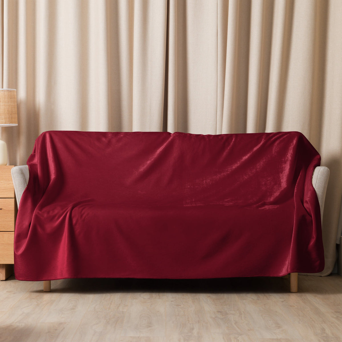 A burgundy sherpa blanket with rich velvet texture drapes elegantly over a modern sofa with soft folds