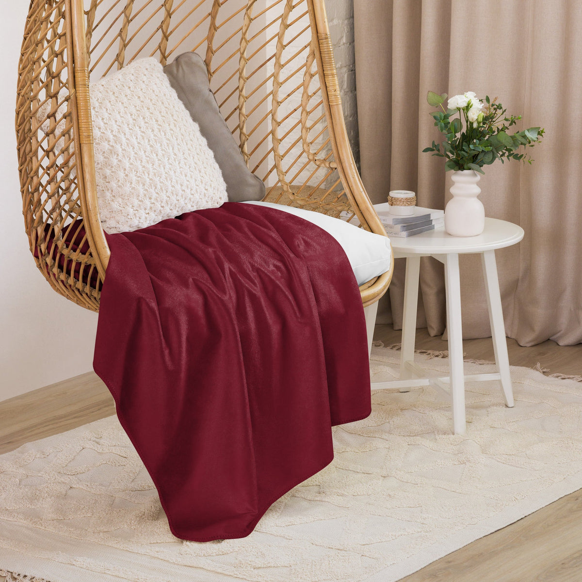 A deep red burgundy sherpa blanket draped over a wicker hanging chair showcasing its plush texture