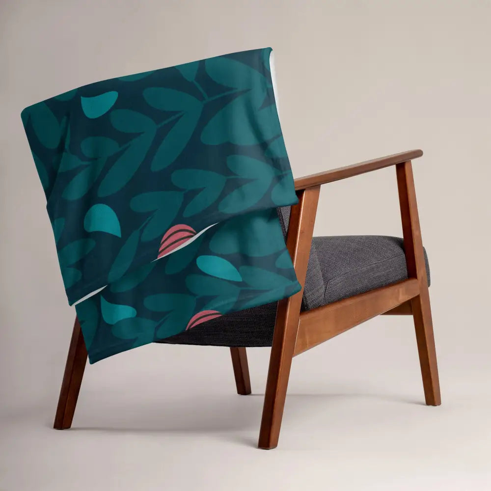 A teal and pink leaf-patterned christmas ornament blanket draped over a wooden armchair