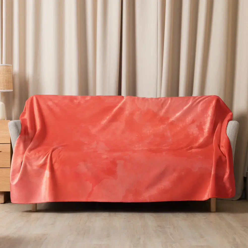Coral sherpa blanket in coral color with plush velvet texture draped over a modern gray armchair back and sides