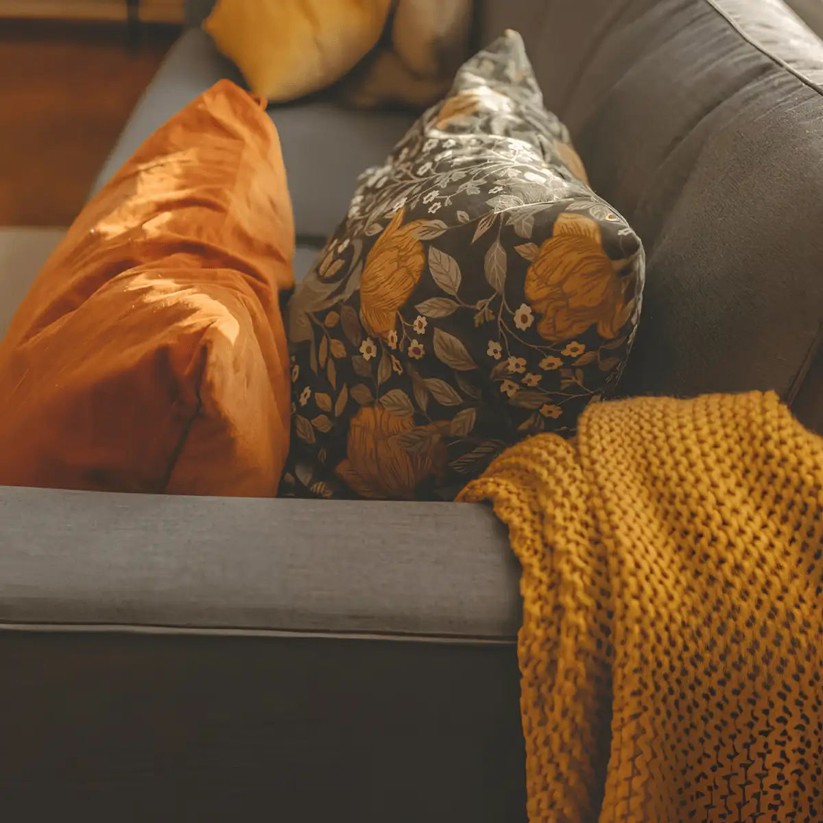A dark gray cushion with a floral pattern in shades of yellow and white, featuring embroidered leaves and blossoms.
