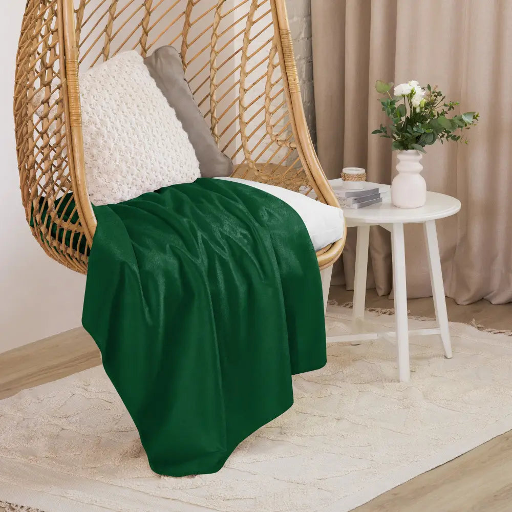 Un plaid sherpa vert foncé en peluche avec une texture douce et veloutée drapé sur une chaise suspendue en osier