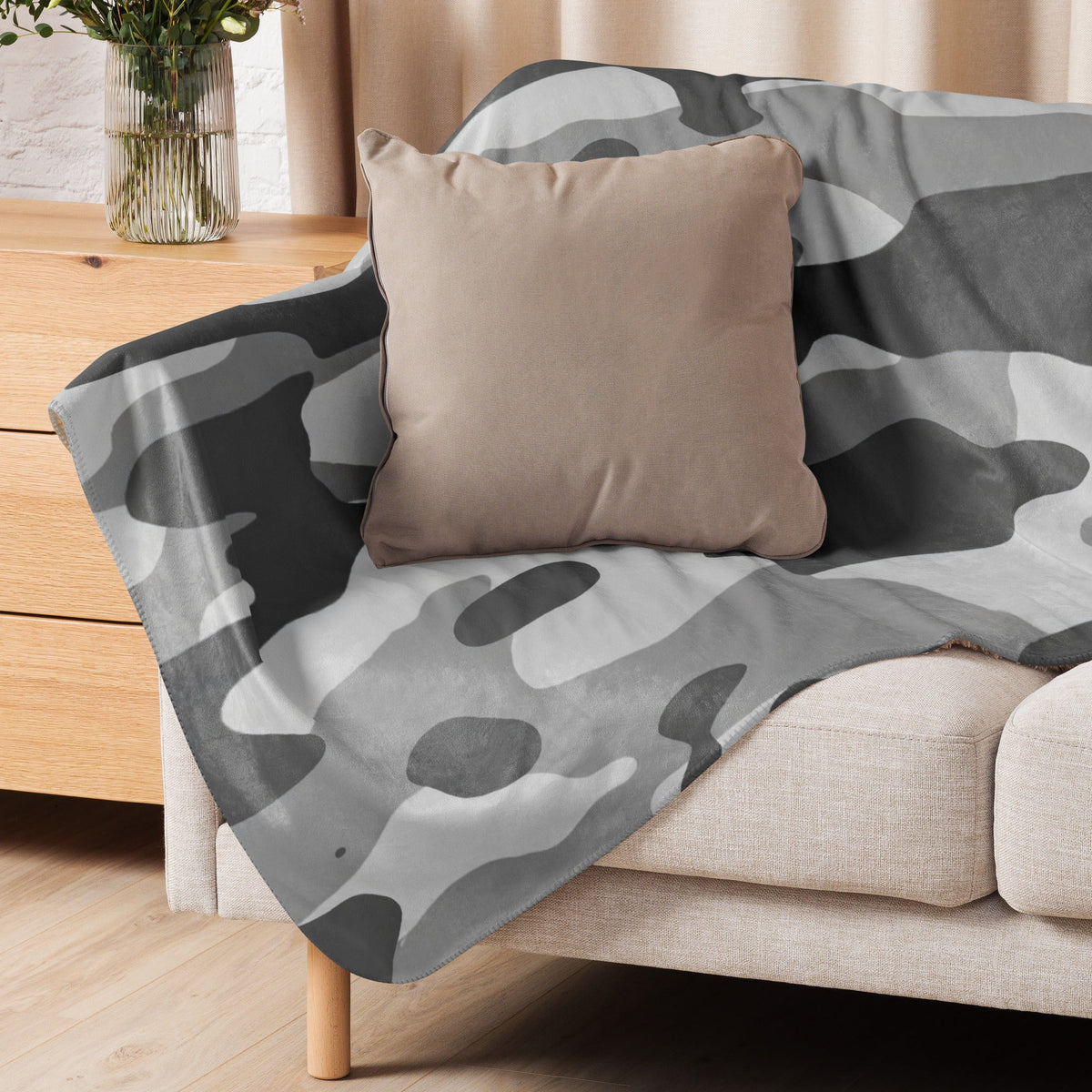 A soft gray camo blanket with a camouflage pattern draped over a beige sofa for cozy home use