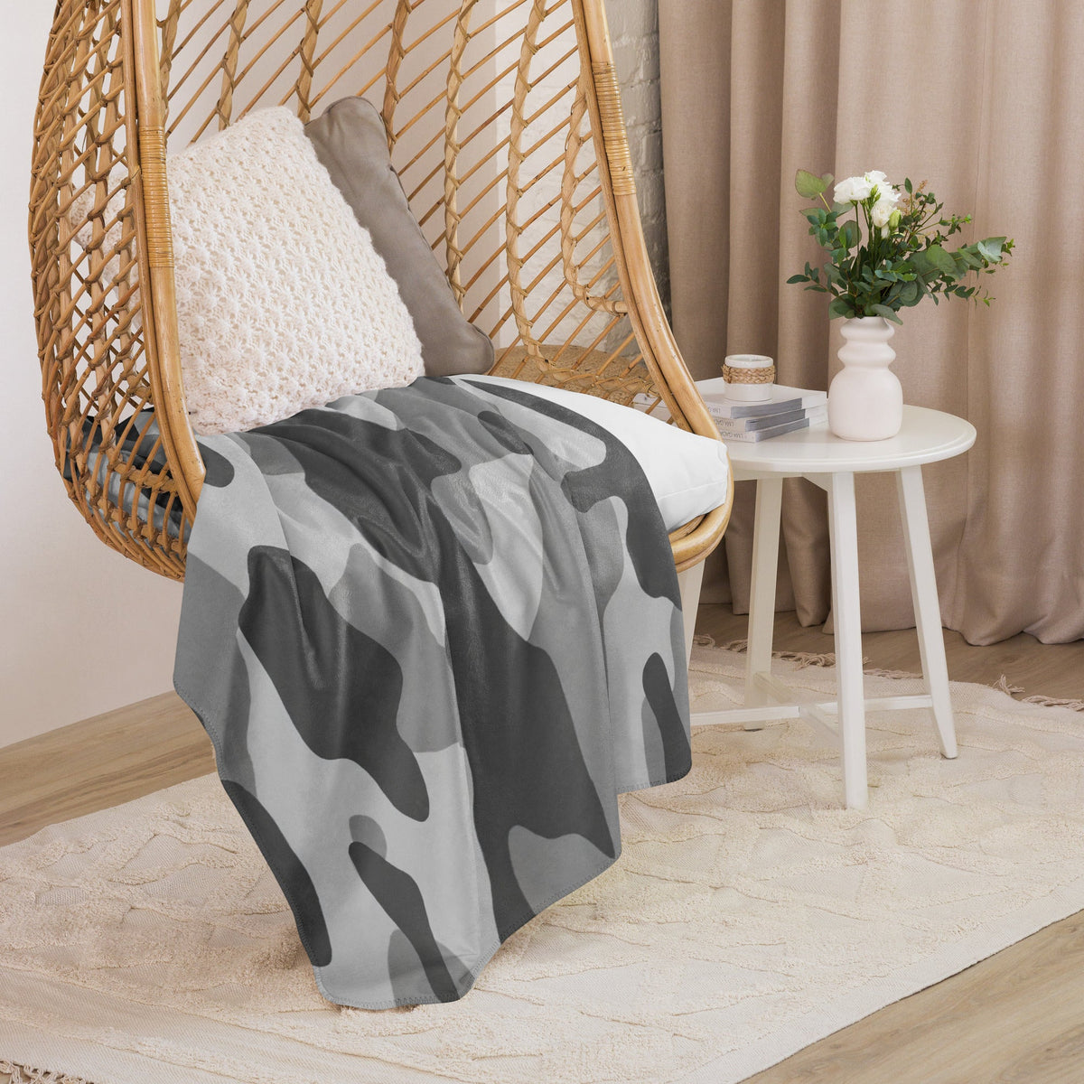 Gray and black camouflage-patterned throw blanket draped over a wicker hanging chair for cozy indoor use