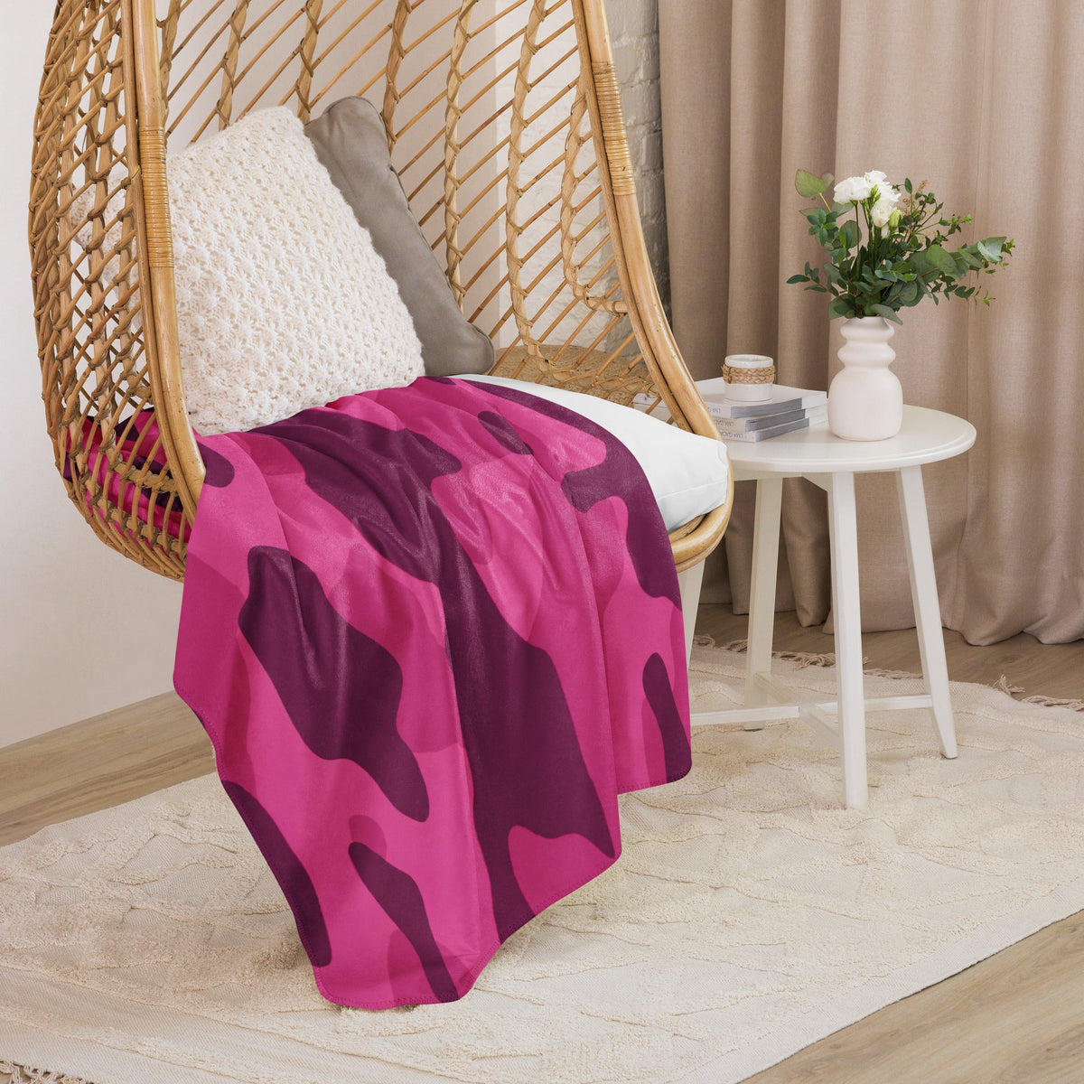 A vibrant hot pink camo blanket with purple camouflage pattern draped over a wicker hanging chair