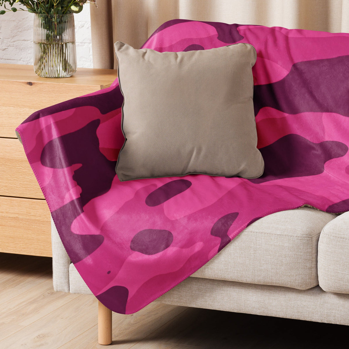 A vibrant hot pink camo blanket with purple camouflage pattern draped over a beige sofa for cozy use