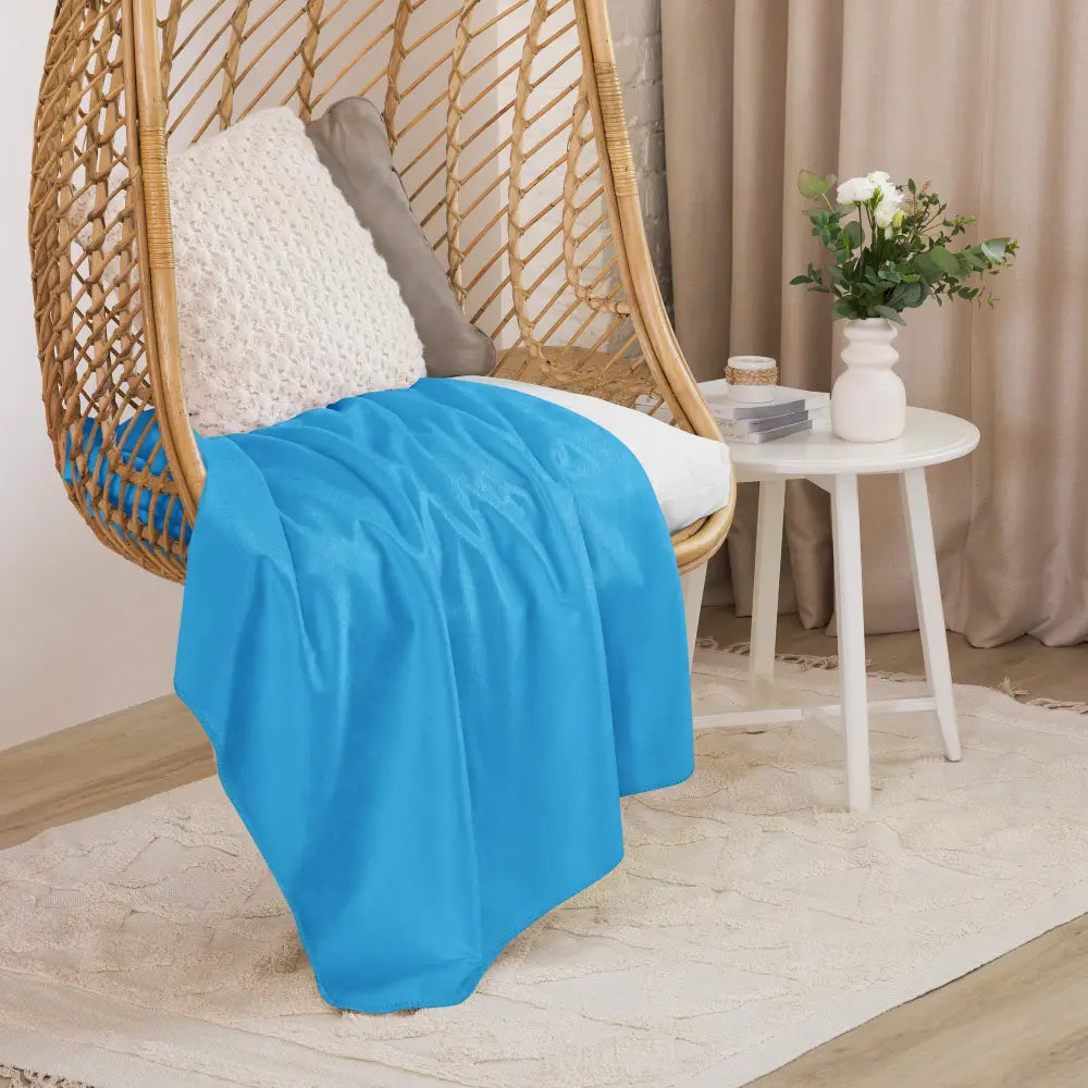 Light blue sherpa blanket made of soft material draped over a wicker hanging chair for cozy comfort