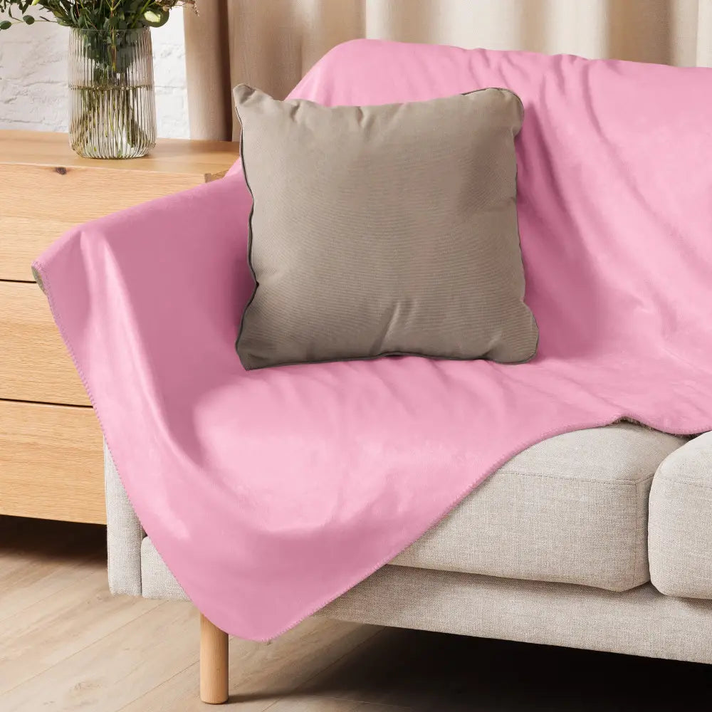 A soft pink sherpa fleece blanket draped over a beige sofa with a taupe pillow resting on it