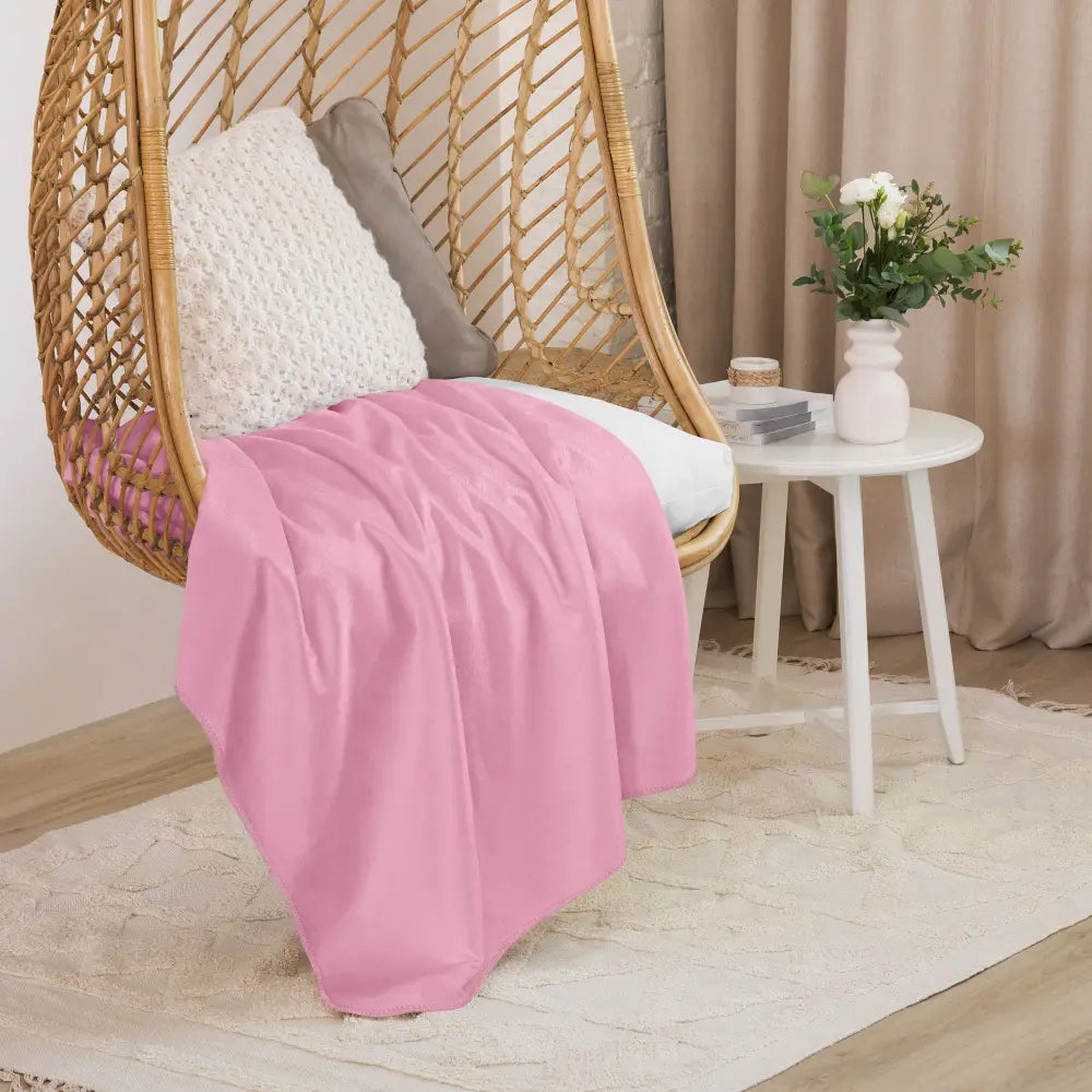 Light pink sherpa blanket made of soft material draped over a wicker hanging chair for cozy comfort
