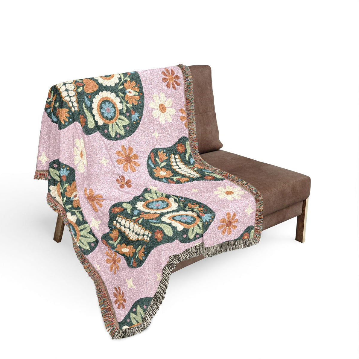 A soft pink Mexican woven blanket with intricate sugar skull designs in dark green orange and blue floral patterns