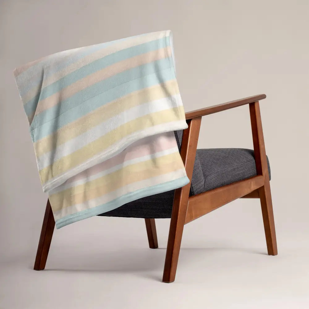 Multicolor striped throw blanket en coton doux pastel avec bandes horizontales bleu clair jaune pâle et blanc sur fauteuil en bois