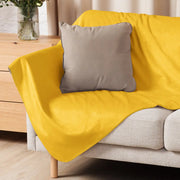 Bright yellow fleece mustard sherpa blanket draped over a sofa showing soft cozy texture and warmth