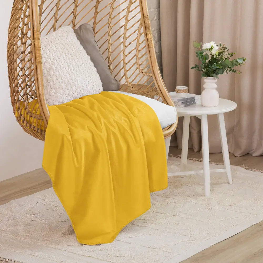 A vibrant mustard sherpa blanket in yellow draped over a wicker hanging chair for cozy comfort
