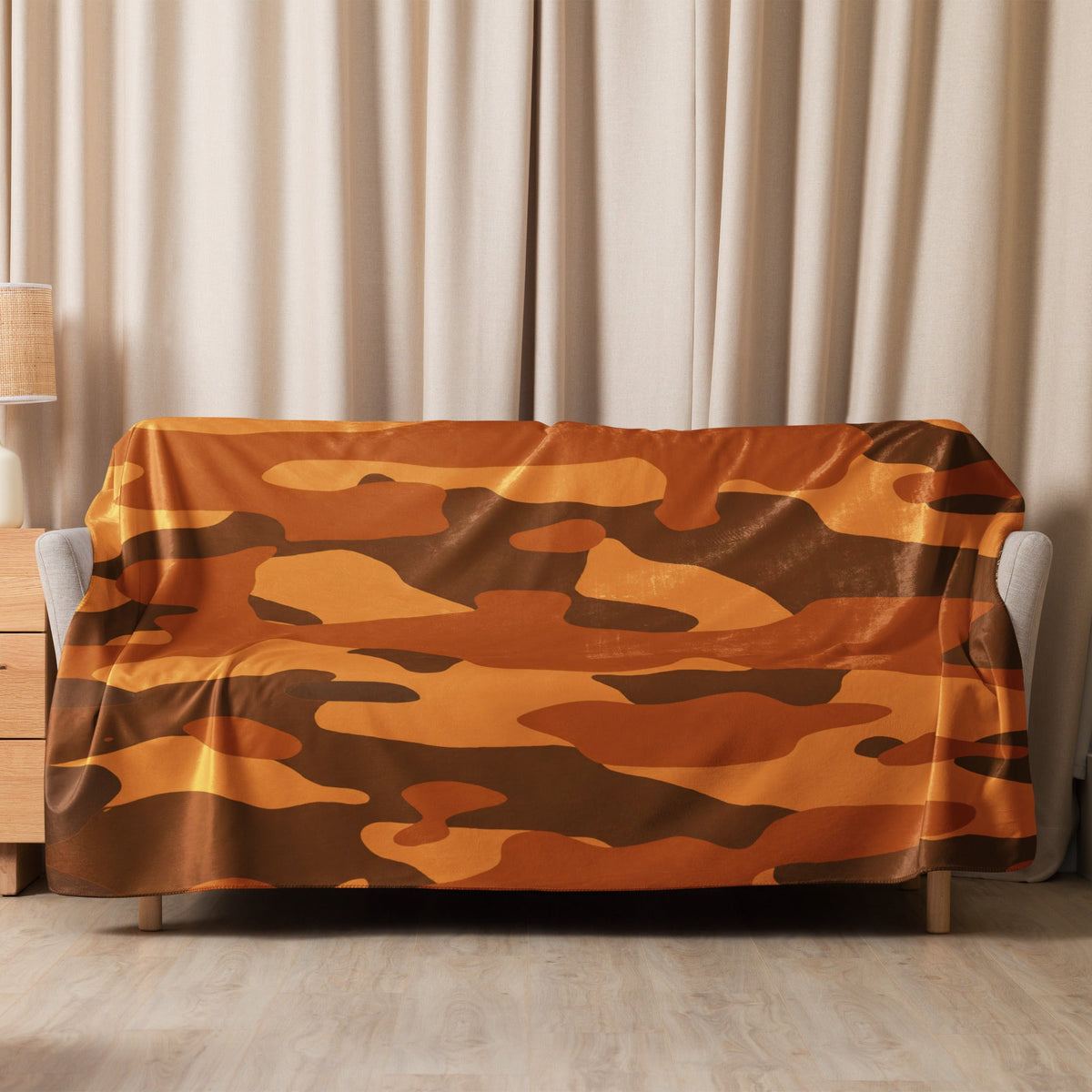 A cozy orange camo blanket with a brown camouflage pattern draped over a modern gray sofa cover