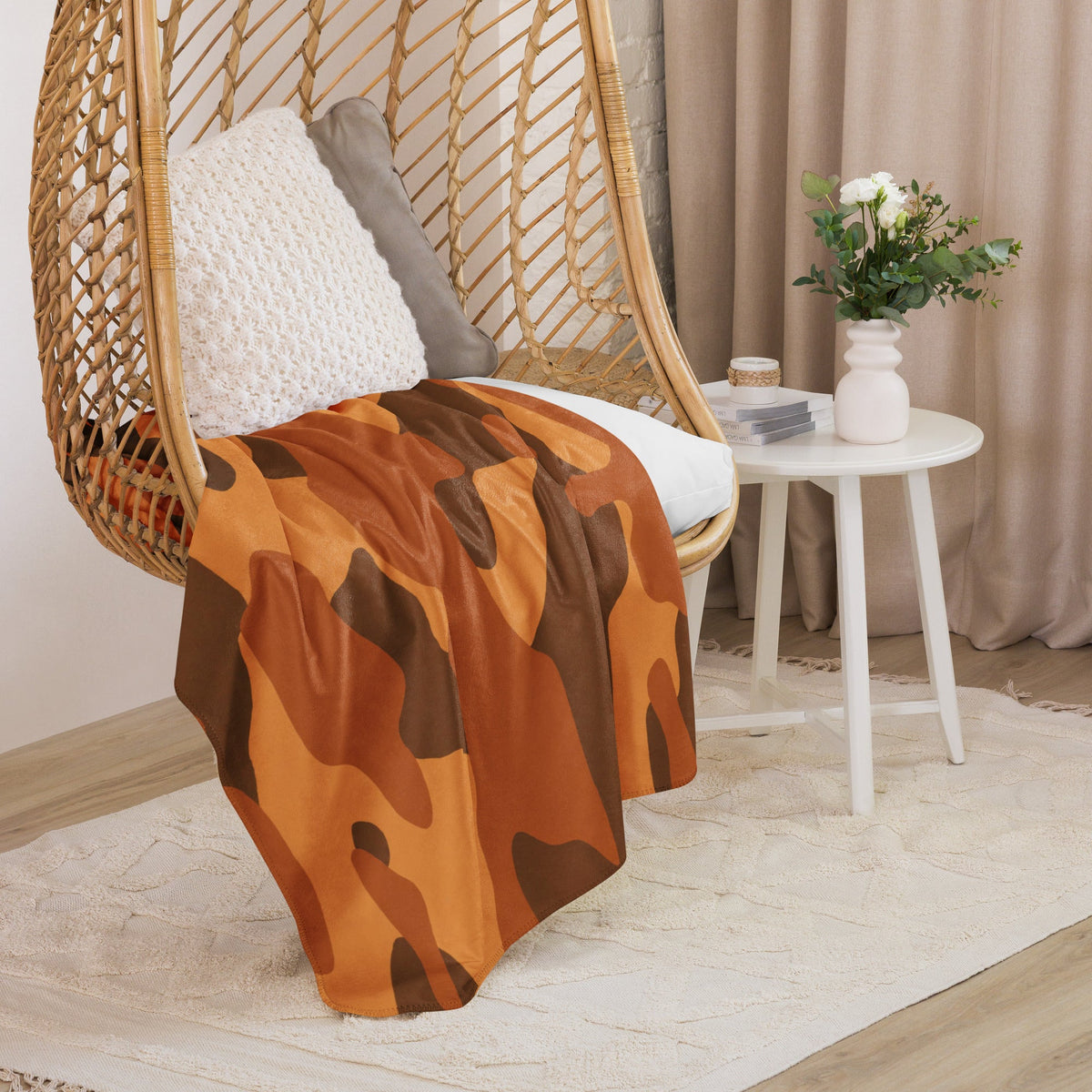 A cozy orange camo blanket with brown patterns draped over a wicker hanging chair for warmth and style