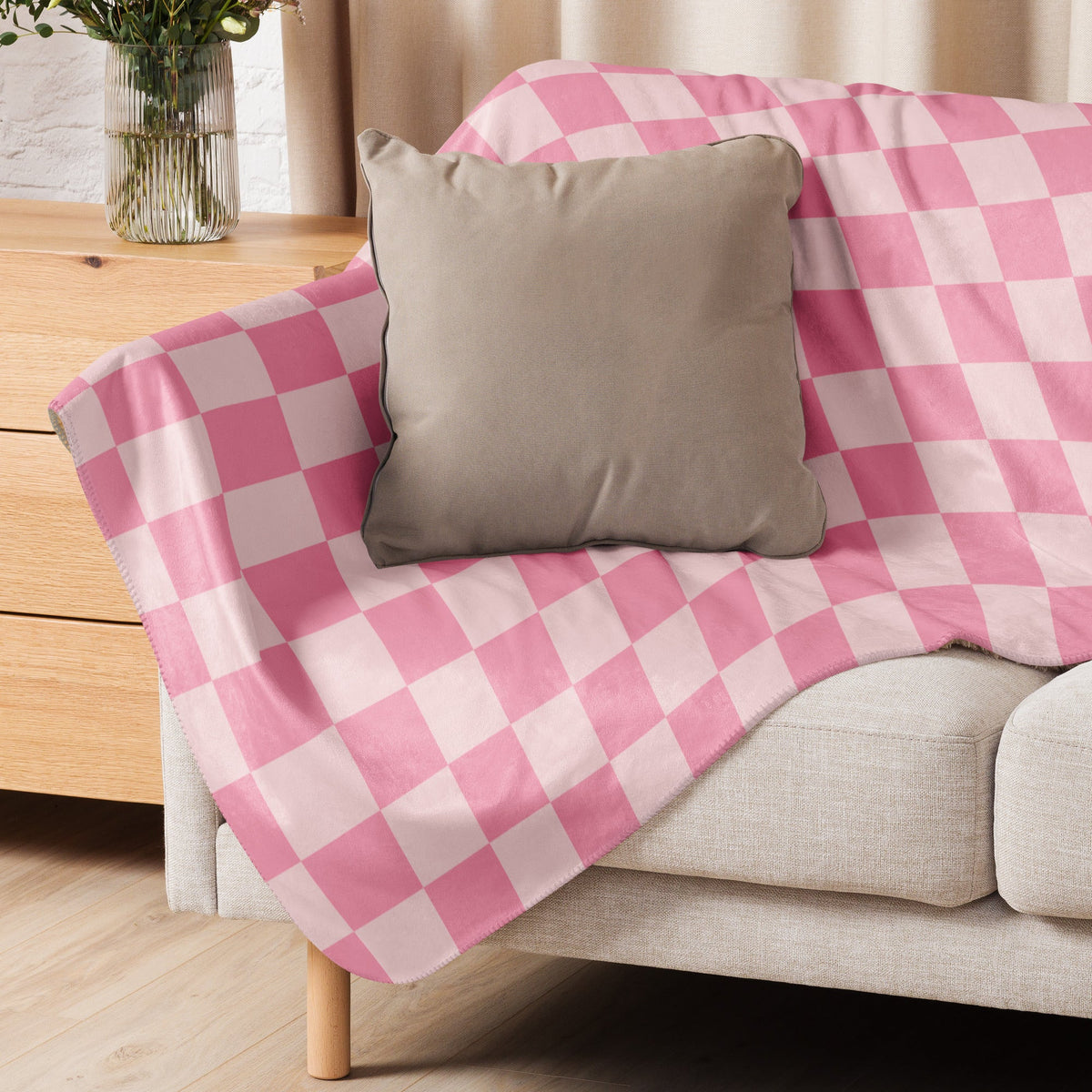 Pink checkered blanket with pink and white pattern draped over a beige sofa showing its front side