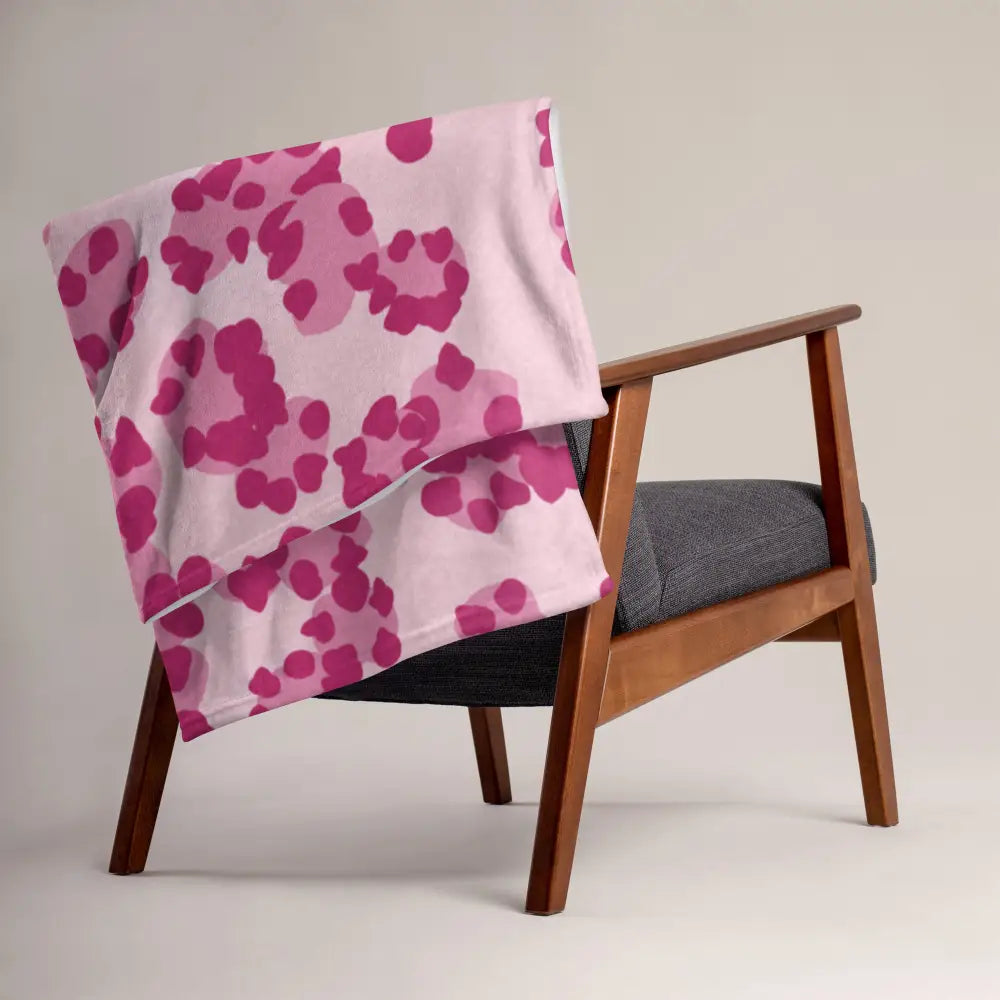 Une couverture douce rose avec un motif léopard rose foncé irrégulier drapée sur le dossier d’un fauteuil en bois