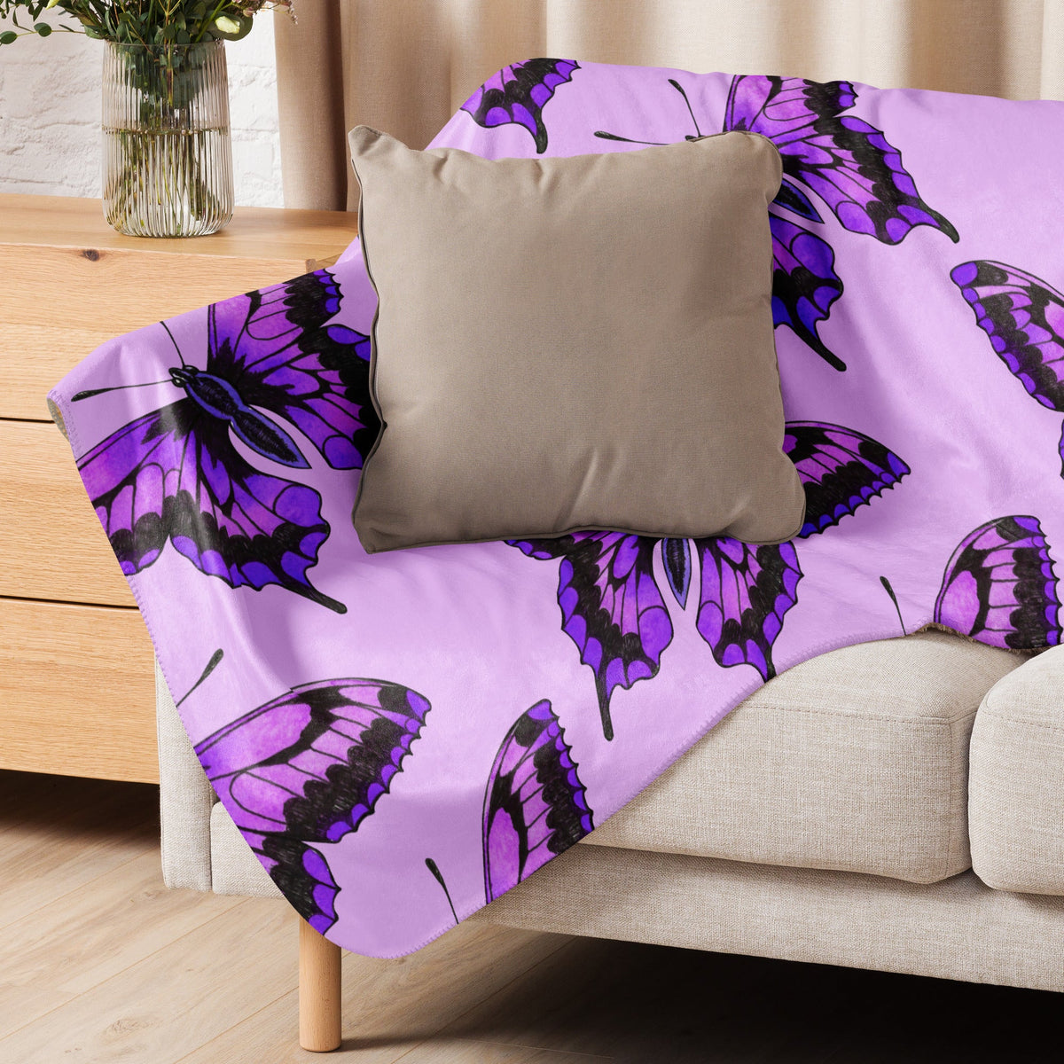 Purple butterfly blanket with black outline pattern draped over beige couch for cozy home use