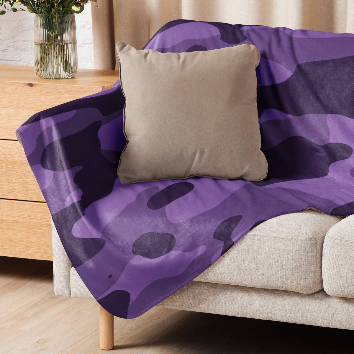Purple camo throw blanket with purple and dark purple camouflage pattern draped over a beige sofa