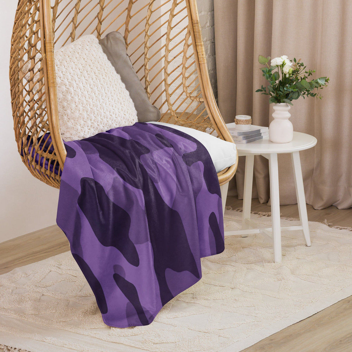 Purple camo throw blanket with dark purple camouflage pattern draped over a wicker hanging chair