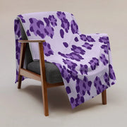A soft white blanket with bold purple leopard print draped over a wooden armchair for cozy use