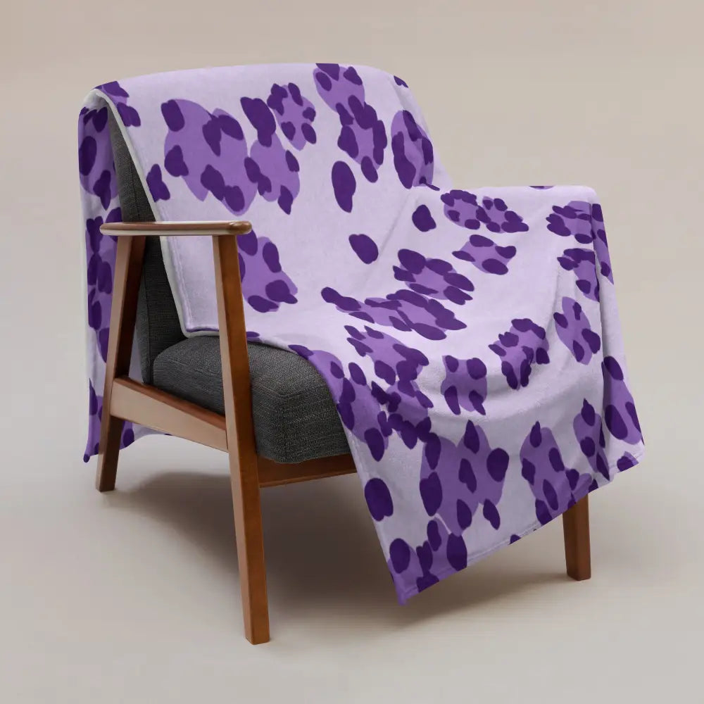 A soft white blanket with bold purple leopard print draped over a wooden armchair for cozy use