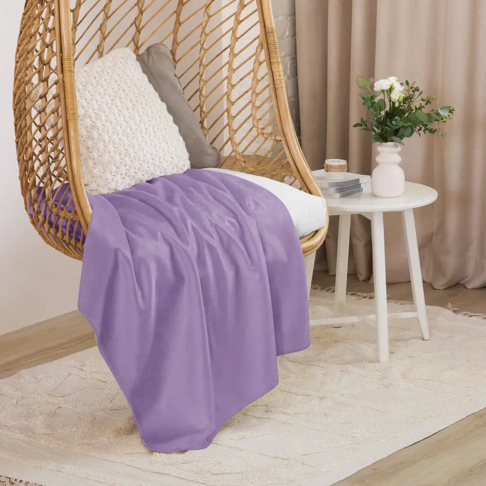 Une couverture sherpa violette douce en lavande drapée sur une chaise suspendue en osier