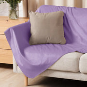 Un plaid sherpa violet doux avec un léger éclat et pliures posé sur un canapé beige