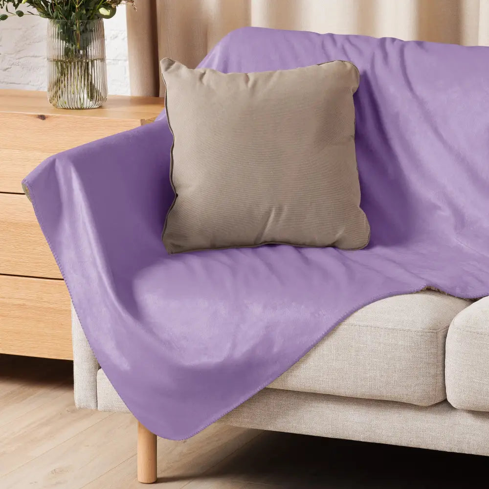 Un plaid sherpa violet doux avec un léger éclat et pliures posé sur un canapé beige