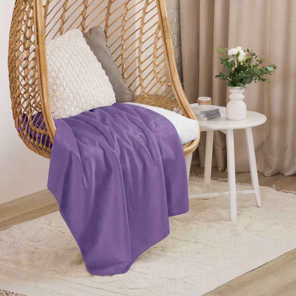 A soft solid purple sherpa throw blanket draped over a wicker hanging chair for cozy comfort