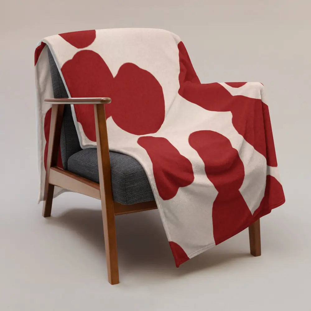 Une couverture rouge et crème en tissu doux avec des formes abstraites rouges sur un fauteuil en bois